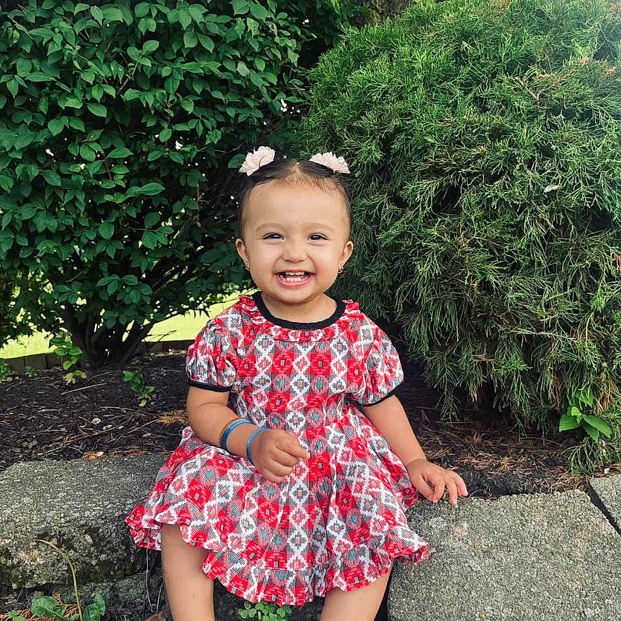 Subella is registered to the contest to win money with this photo: anklet, bush, child, cute, dress, garden, greenery, hair_accessories, happy, nature, outdoor, playful, portrait, sandals, sitting, smiling, stone, sunlight, toddler, tree