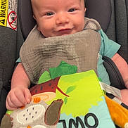 Ajay is registered to the contest to win money with this photo: baby, infant, car_seat, bib, toy, fabric_book, owl, green, blue, gray, smiling, child, cute, young, indoors, portrait, happy, seated, clothing, play