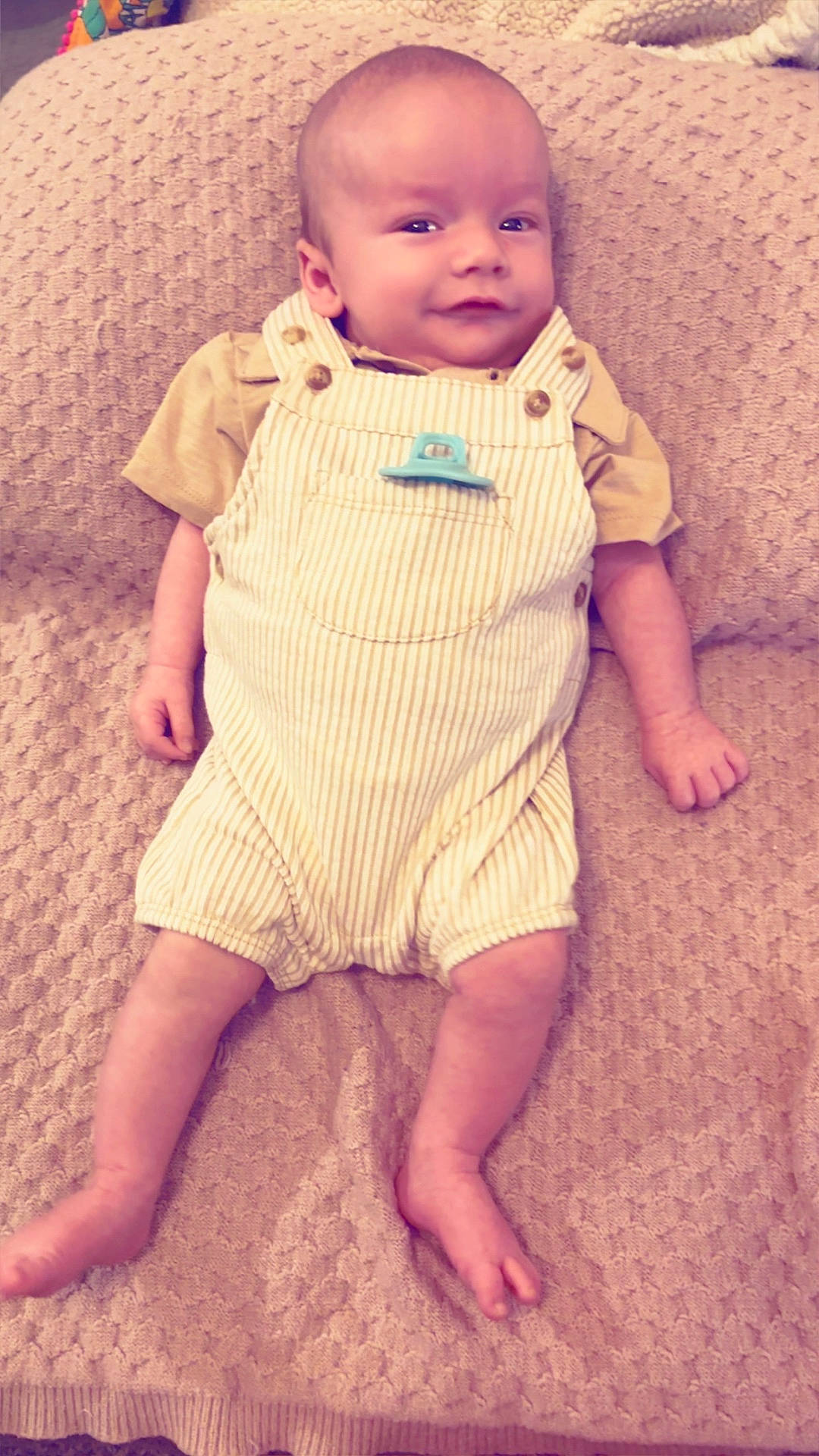 baby, beige_blanket, child, clothing, cute, face, furniture, head, indoors, infant, lying_down, overalls, person, relaxed, skin, small_feet, small_hands, smile, striped_clothing, texture