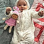baby, child, doll, blanket, quilt, onesie, hat, toy, infant, soft, cute, lying_down, pink, white, patterned, fabric, nursery, indoor, person, smiling