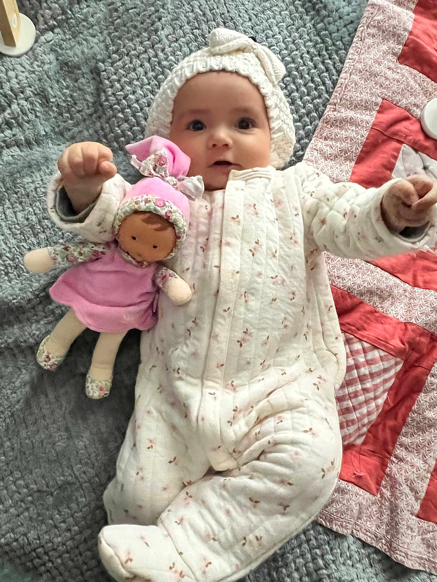 Hélya participe au concours pour gagner de l'argent avec cette photo : baby, child, doll, blanket, quilt, onesie, hat, toy, infant, soft, cute, lying_down, pink, white, patterned, fabric, nursery, indoor, person, smiling