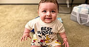 Princeton is registered to the contest to win money with this photo: baby, child, smiling, sitting, indoor, carpet, tshirt, mickey_mouse, pluto, clothing, cute, happy, person, infant, young_child, home, floor, shorts, cartoon_characters, playful