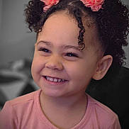 Zamyiah is registered to the contest to win money with this photo: cheeks, child, closeup, curly_hair, cute, expression, eyelashes, face, hair_accessory, happy, indoors, joyful, person, pink_flower, pink_shirt, portrait, skin, smile, toddler, young_child