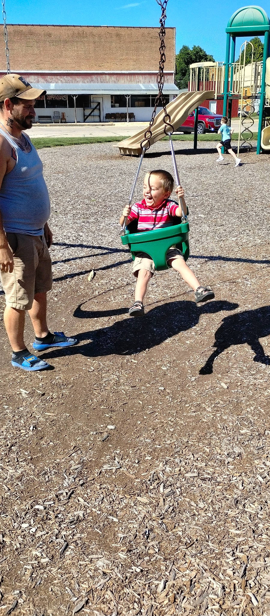 Jordan is registered to the contest to win money with this photo: asphalt, child, city, event, fun, grass, headwear, leisure, outdoor_play_equipment, people_in_nature, person, plant, play, playground, recreation, shorts, soil, swing, t_shirt, toddler