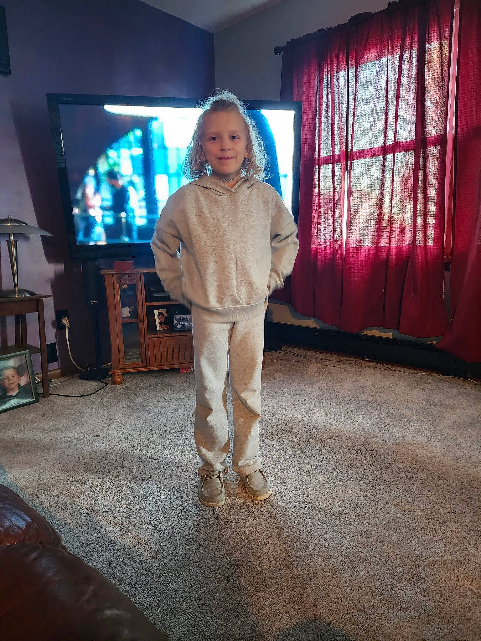 Lynnlee is registered to the contest to win money with this photo: curtain, display_device, entertainment_center, event, fashion_design, flash_photography, flooring, hardwood, home_appliance, human_leg, joy, knee, led_backlit_lcd_display, person, room, smile, standing, television, television_set, toddler