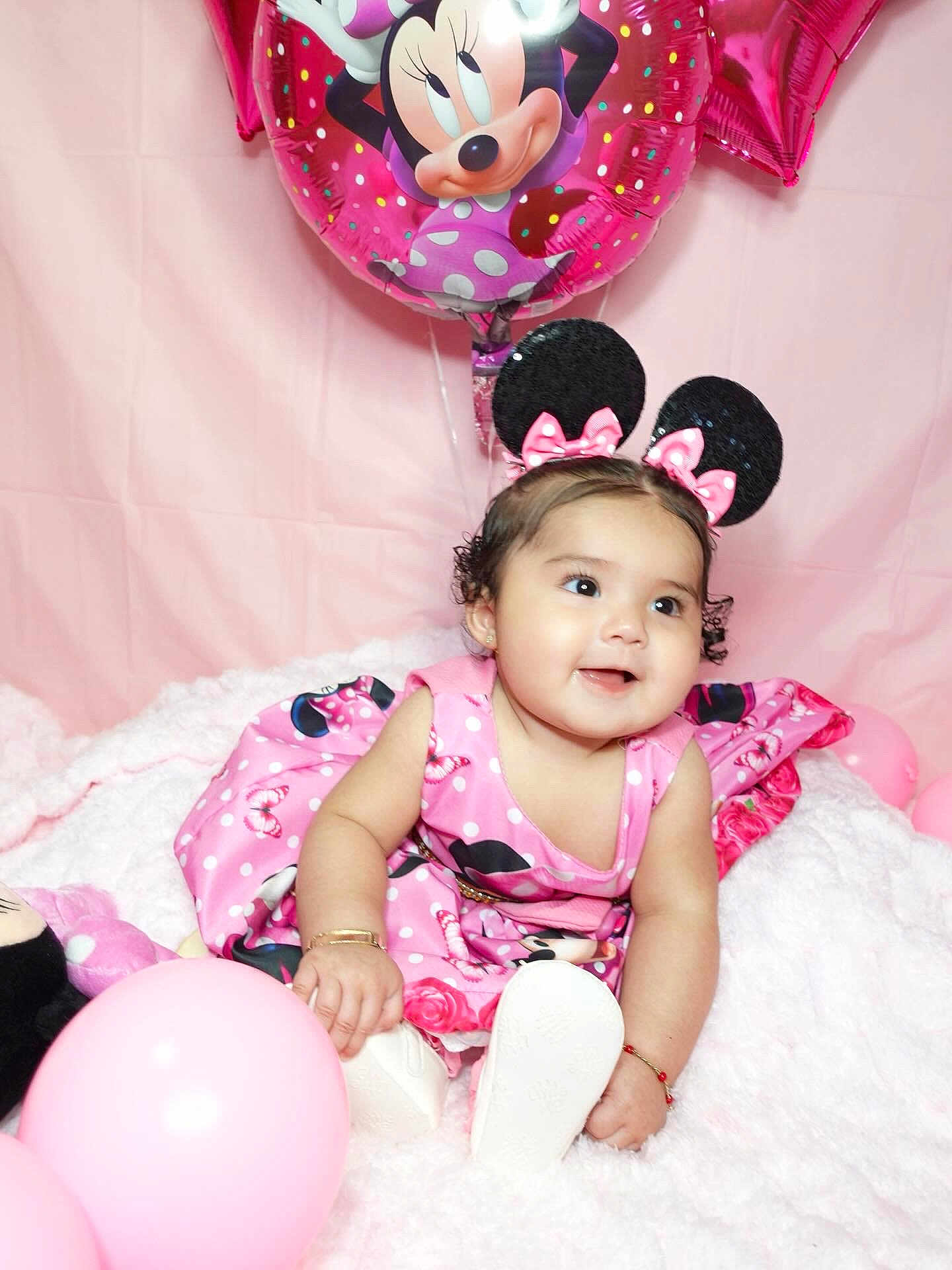 Laylah is registered to the contest to win money with this photo: baby, child, pink, balloon, minnie_mouse, dress, headband, mouse_ears, smile, fluffy_blanket, celebration, cute, indoor, toy, happy, birthday, accessory, sitting, infant, party