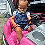 toddler, child, pacifier, toy_car, pink, steering_wheel, outdoor, sunny, concrete, garage, car, denim_overall, shorts, hair_clip, baby, seatbelt, play, person, daytime, casual