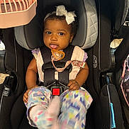 Brilani is registered to the contest to win money with this photo: baby, car_seat, child, infant, headband, bow, pacifier, colorful_clothing, straps, black_car_seat, pink_fan, baby_clothes, seatbelt, playful_expression, indoor, closeup, cute, child_safety, infant_fashion, baby_feet
