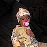 baby, pacifier, pajamas, hat, infant, cute, sleepwear, bear_pattern, hand, face, child, newborn, clothing, lying_down, indoors, soft_toys, blanket, dark_background, sleep, comfort
