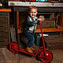 Kameron joined the competition — help win amazing prizes! toddler, child, scooter, red, boots, plaid_shirt, workshop, tools, wooden_crate, toy_cars, face, smile, floor, cabinet, doll, rustic, indoor, boy, standing, vintage