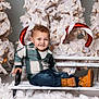 child, toddler, bench, plaid_shirt, jeans, boots, christmas_tree, candy_cane, holiday, snow, decorations, smile, happy, indoor, seasonal, festive, white, green, red, portrait