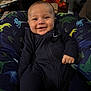 baby, smiling, child, onesie, blue_clothing, dinosaur_pattern, cushion, indoor, flowers, homedecor, happy, portrait, infant, seated, cozy, cute, person, face, young, comfortable