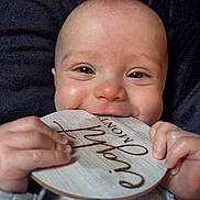 Atticus joined the competition — help win amazing prizes! baby, infant, child, hands, wooden_plaque, milestone, smile, closeup, face, eyes, skin, clothing, blanket, texture, cute, portrait, teething, happy, indoor, person