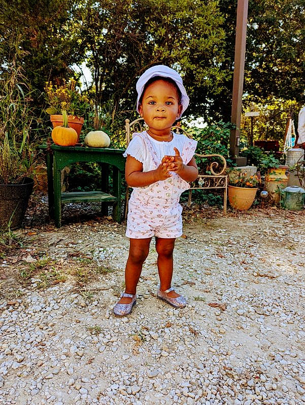 Zariyah is registered to the contest to win money with this photo: baby_toddler_clothing, botany, child, flowerpot, foot, fruit, fun, grass, happy, hat, houseplant, leisure, people_in_nature, person, plant, sitting, smile, sun_hat, toddler, tree