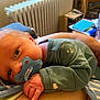 Noah is registered to the contest to win money with this photo: newborn, baby, pacifier, infant, hand, face, sleeping, resting, clothing, green_sleeve, person, closeup, indoor, radiator, table, cup, books, handheld, comfort, home