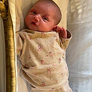 Gypsi-Ami is registered to the contest to win money with this photo: baby, infant, clothing, ribbed_fabric, floral_pattern, basket, cushion, soft_light, shadow, lying_down, head, face, hand, foot, skin, bed, resting, curious, indoors, portrait