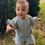 Arlette is registered to the contest to win money with this photo: toddler, child, grass, outdoor, greenery, curly_hair, blue_outfit, sandals, cute, standing, smiling, young_child, nature, daylight, portrait, person, small_child, playful, summer_clothing, happy