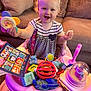 Riley is registered to the contest to win money with this photo: toddler, child, baby, walker, toy, smiling, indoor, couch, curly_hair, snack, colorful, plastic_toy, striped_dress, pink, playtime, happy, seated, activity_center, person, living_room