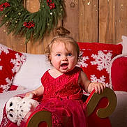 Ysalia participe au concours pour gagner de l'argent avec cette photo : child, christmas, christmas_tree, cozy, curly_hair, decorations, festive, happy, holiday, indoor, owl, pillows, plush_toy, red_dress, sitting, smiling, snowflake_pattern, toddler, wooden_background, wreath