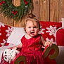 child, christmas, christmas_tree, cozy, curly_hair, decorations, festive, happy, holiday, indoor, owl, pillows, plush_toy, red_dress, sitting, smiling, snowflake_pattern, toddler, wooden_background, wreath