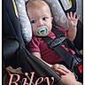 baby, infant, child, car_seat, safety_harness, pacifier, waving, blue_eyes, sitting, portrait, indoor, vehicle, pink_clothing, cushion, padded_seat, text_overlay, name_text, year_text, close_up, safe