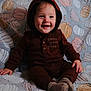 baby, child, smiling, hoodie, brown_clothing, sitting, blanket, pumpkin_pattern, cozy, indoors, cute, happy, face, portrait, infant, soft_texture, warm_clothing, toddler, playful, young_child