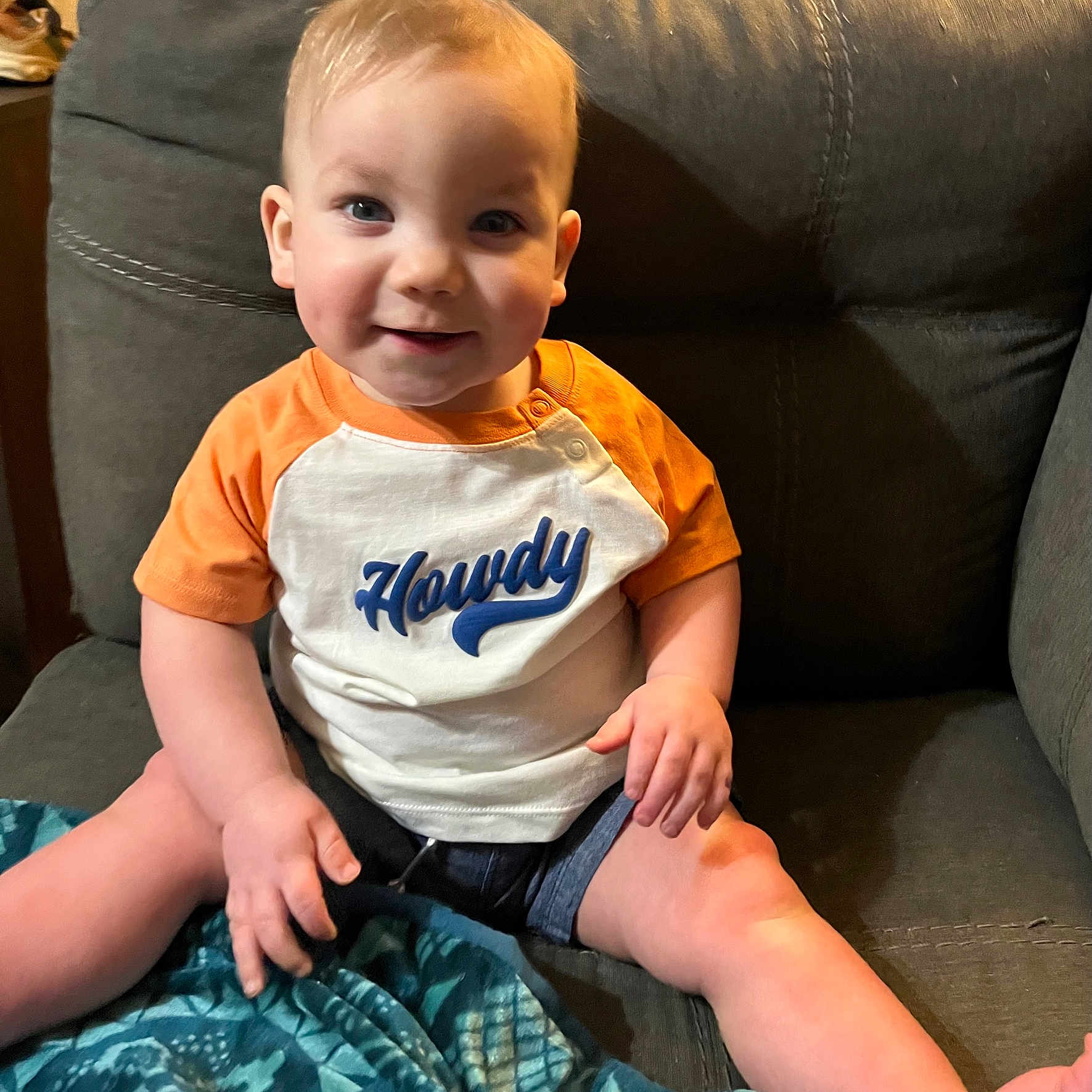 Charles joined the competition — help win amazing prizes! baby, blanket, blue_eyes, casual_clothing, child, couch, cute, fabric, face, hand, happy, home, indoor, legs, orange_shirt, person, shorts, sitting, smiling, toddler