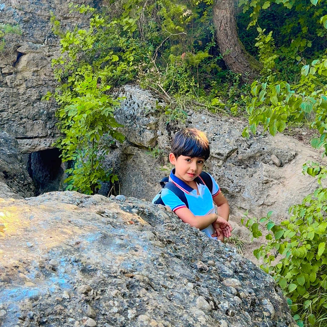 Muhamad Ibrahim participe au concours pour gagner de l'argent avec cette photo : adventure, backpack, boy, casual_clothing, child, curious, daylight, exploration, forest, greenery, leaves, natural_light, nature, outdoor, plants, rock, scenery, smiling, trees, young