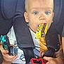 toddler, child, car_seat, toy_cars, yellow_school_bus, red_car, blue_eyes, seatbelt, clothing, white_shirt, yellow_shorts, hand, mouth, face, baby, straps, indoor, person, cute, playing