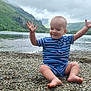 toddler, child, lake, rocks, outdoor, nature, water, hill, cloudy_sky, blue_clothing, barefoot, smiling, grass, landscape, summer, scenic, recreation, playful, casual, happy