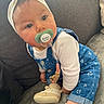 Yvanah participe au concours pour gagner de l'argent avec cette photo : baby, child, pacifier, headband, blue_overalls, white_shirt, couch, indoor, soft_lighting, curious_expression, footwear, sock, seated, cute, infant, face, person, clothing, toy, home