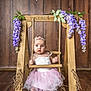 baby, child, swing, wooden_swing, flower_headband, pink_dress, white_dress, purple_flowers, white_flowers, wooden_background, floor, ropes, cute, portrait, indoor, decorative_flowers, infant, sitting, barefoot, baby_girl