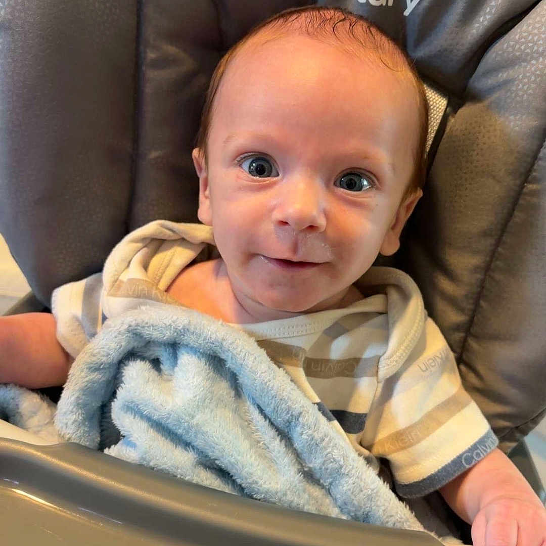 Bentley is registered to the contest to win money with this photo: baby, high_chair, blanket, blue, infant, smile, face, person, clothing, striped_shirt, indoor, seat, cute, child, young, happy, skin, head, expression, comfort