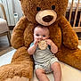 baby, teddy_bear, plush_toy, nursery, child, infant, wooden_sign, floor_rug, soft_toy, cute, smiling, indoor, childrens_room, baby_clothes, striped_outfit, furniture, carpet, toy, happy, portrait