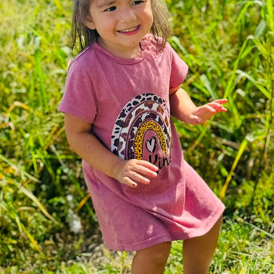 Waverly is registered to the contest to win money with this photo: casual_clothing, child, cute, daylight, footwear, grass, greenery, happy, nature, outdoor, person, pink_dress, portrait, rainbow_design, smiling, standing, sunny_day, toddler, white_sandals, young_child