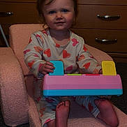 Harper-Grace is registered to the contest to win money with this photo: child, toddler, pajamas, heart_pattern, toy_keyboard, pink_chair, foam_chair, bare_feet, portrait, smile, indoor, dresser, drawer_handles, hanger, carpet, furniture, playtime, young_child, person, bedtime