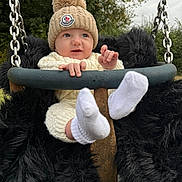 Arthur joined the competition — help win amazing prizes! baby, child, swing, knit_hat, pom_pom, white_socks, knit_outfit, outdoor, trees, grass, metal_chains, black_fur_padding, cute, infant, playground, park, smiling, person, nature, cold_weather