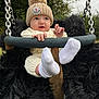 baby, child, swing, knit_hat, pom_pom, white_socks, knit_outfit, outdoor, trees, grass, metal_chains, black_fur_padding, cute, infant, playground, park, smiling, person, nature, cold_weather