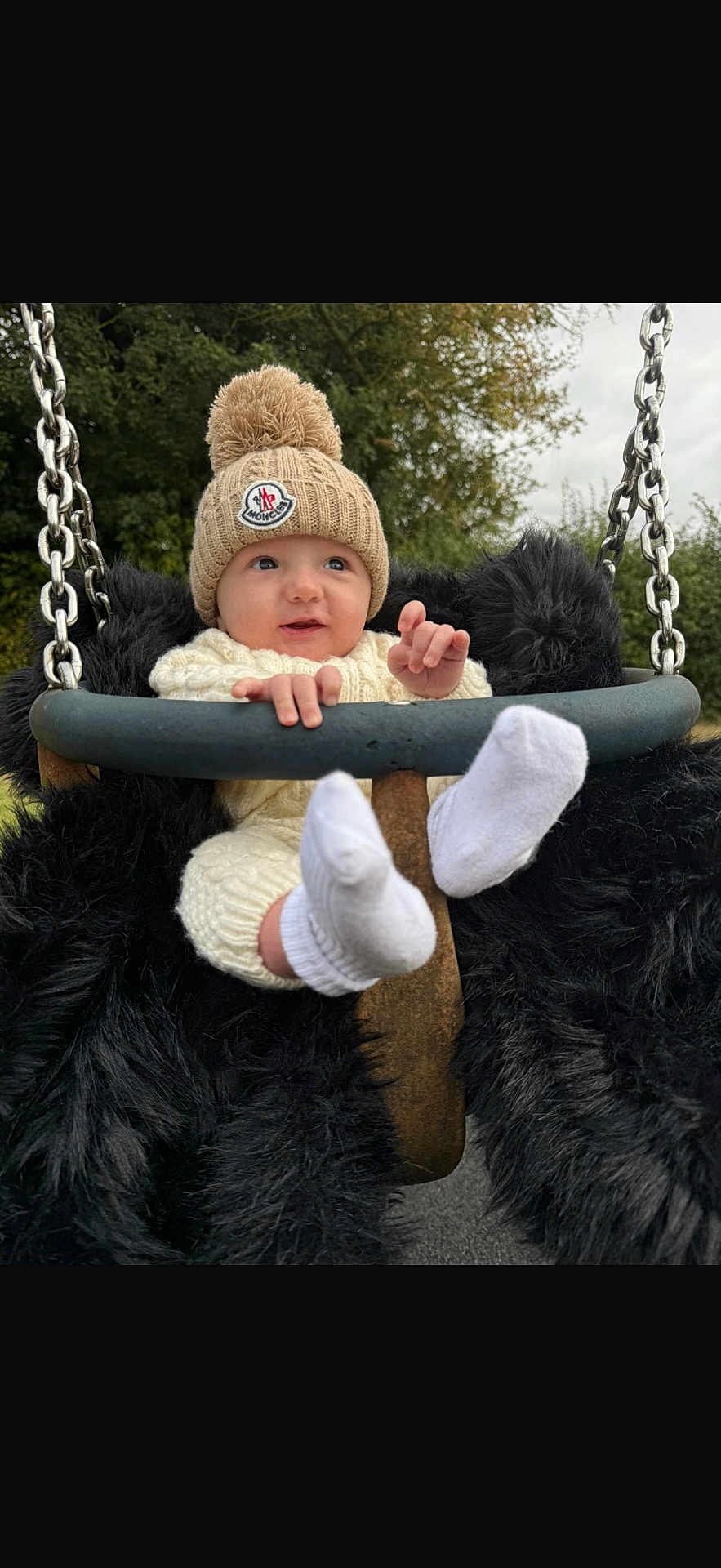 Arthur joined the competition — help win amazing prizes! baby, child, swing, knit_hat, pom_pom, white_socks, knit_outfit, outdoor, trees, grass, metal_chains, black_fur_padding, cute, infant, playground, park, smiling, person, nature, cold_weather