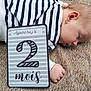 baby, sleeping, striped_clothing, denim, carpet, milestone_card, age_card, hand, face, infant, newborn, side_view, resting, cute, child, soft_texture, indoor, closeup, portrait, peaceful