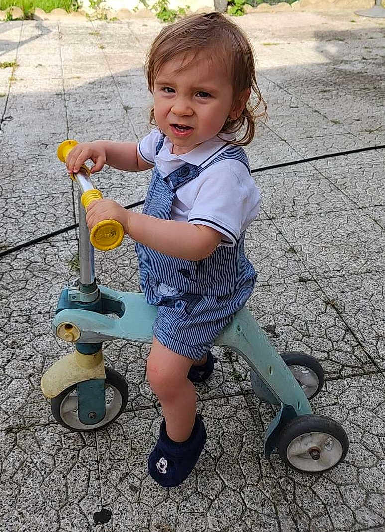 Kassim participe au concours pour gagner de l'argent avec cette photo : toddler, child, scooter, outdoor, play, footwear, expression, romper, mickey_mouse, toy, pavement, concrete, summer, sunlight, casual, vehicle, transport, person, fun, activity