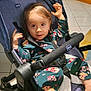toddler, child, stroller, pajamas, indoor, curtains, floor_tiles, furniture, baby, footwear, face, hands, smile, black_stroller, blanket, patterned_clothing, chicco_brand, curly_hair, seated, home