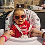 Kassim a rejoint le concours — aidez-le/la à gagner de superbes lots ! baby, child, high_chair, sunglasses, red_clothing, kitchen, toy, ball, car_toy, hand_holding, smiling, indoor, person, furniture, seat, happy, face, glasses, table, home