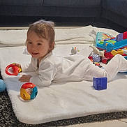 Kassim a rejoint le concours — aidez-le/la à gagner de superbes lots ! baby, child, indoor, blanket, toy, colorful, pajamas, floor, couch, window, happy, smiling, play, soft, carpet, white, gray, tiled_floor, infant, young_child