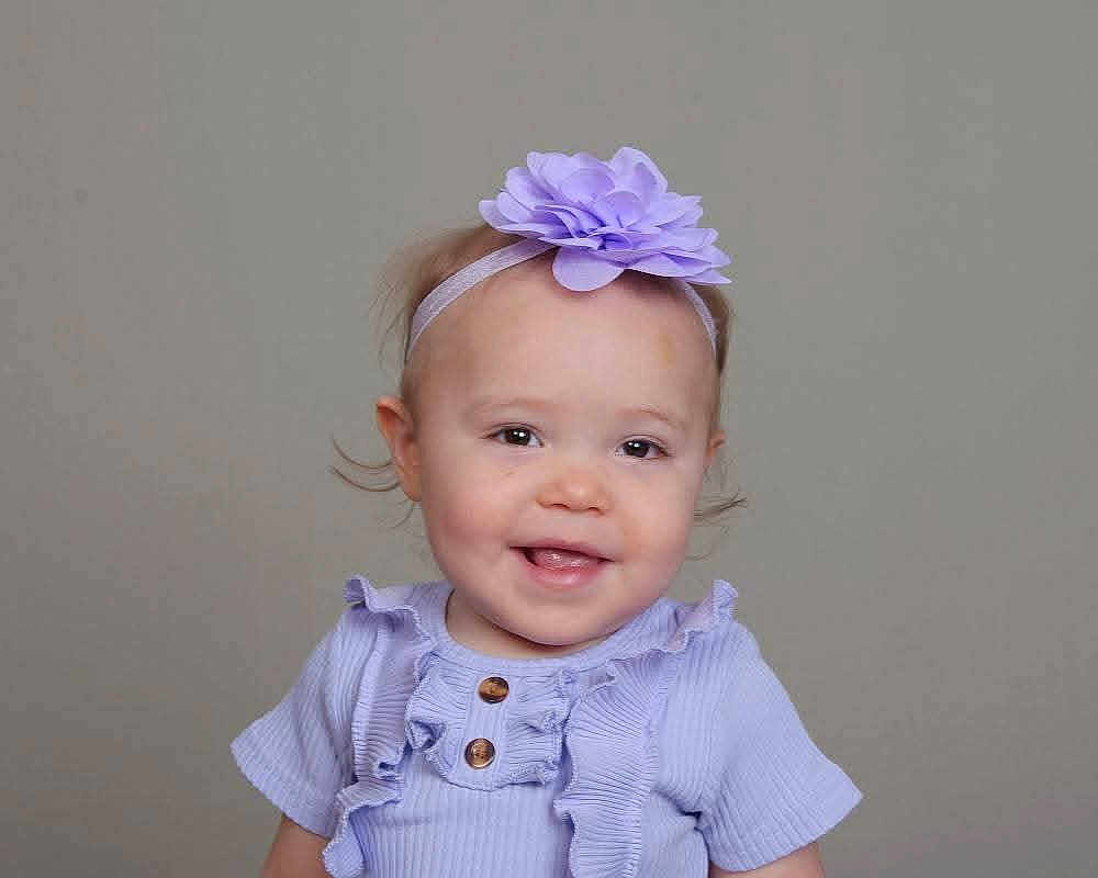 Odessa is registered to the contest to win money with this photo: baby, child, girl, headband, flower, smile, portrait, clothing, purple, ruffles, cute, happy, face, infant, young_child, studio, neutral_background, headwear, fashion, toddler