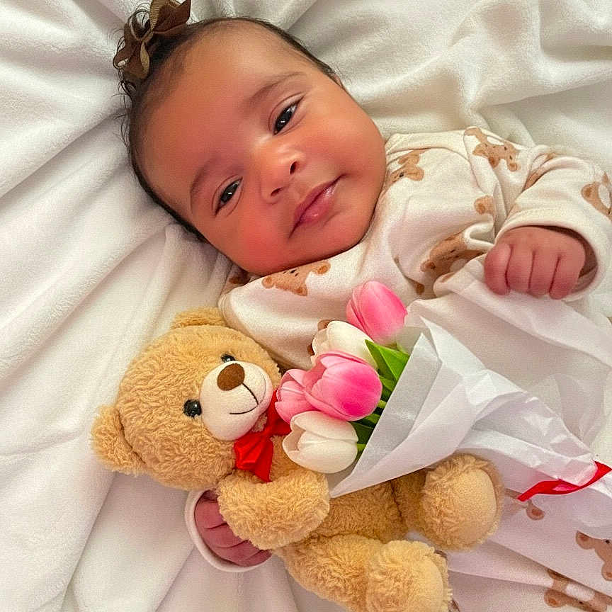 Zionna joined the competition — help win amazing prizes! baby, bed, blanket, bow, closeup, cozy, cute, flowers, hand, happy, infant, laying_down, nursery, onesie, plush, portrait, smile, soft_toy, teddy_bear, tulips