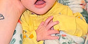 Ezrah is registered to the contest to win money with this photo: baby, infant, yellow_clothing, blanket, hand, face, wide_eyes, surprised_expression, soft_texture, floral_pattern, cradled, cozy, cute, newborn, person, skin, indoors, warm, comfort, portrait
