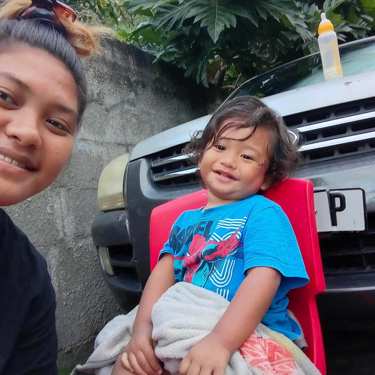 Temeio a rejoint le concours — aidez-le/la à gagner de superbes lots ! blanket, blue_shirt, car, casual_clothing, child, concrete_wall, curly_hair, daylight, family, grass, happy, nature, outdoor, person, portrait, red_chair, smile, toddler, vehicle, woman