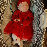 Cecilia is registered to the contest to win money with this photo: baby, sleeping, red_dress, headband, baby_seat, patterned_fabric, tights, heart_pattern, infant, cozy, indoors, child, cute, resting, soft_lighting, portrait, small_hands, peaceful, comfort, adorable