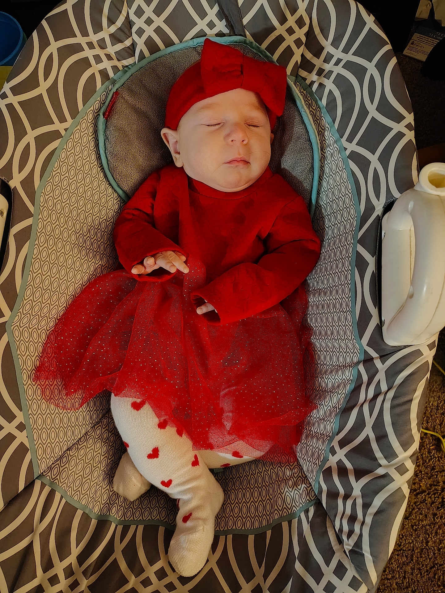 Cecilia is registered to the contest to win money with this photo: baby, sleeping, red_dress, headband, baby_seat, patterned_fabric, tights, heart_pattern, infant, cozy, indoors, child, cute, resting, soft_lighting, portrait, small_hands, peaceful, comfort, adorable